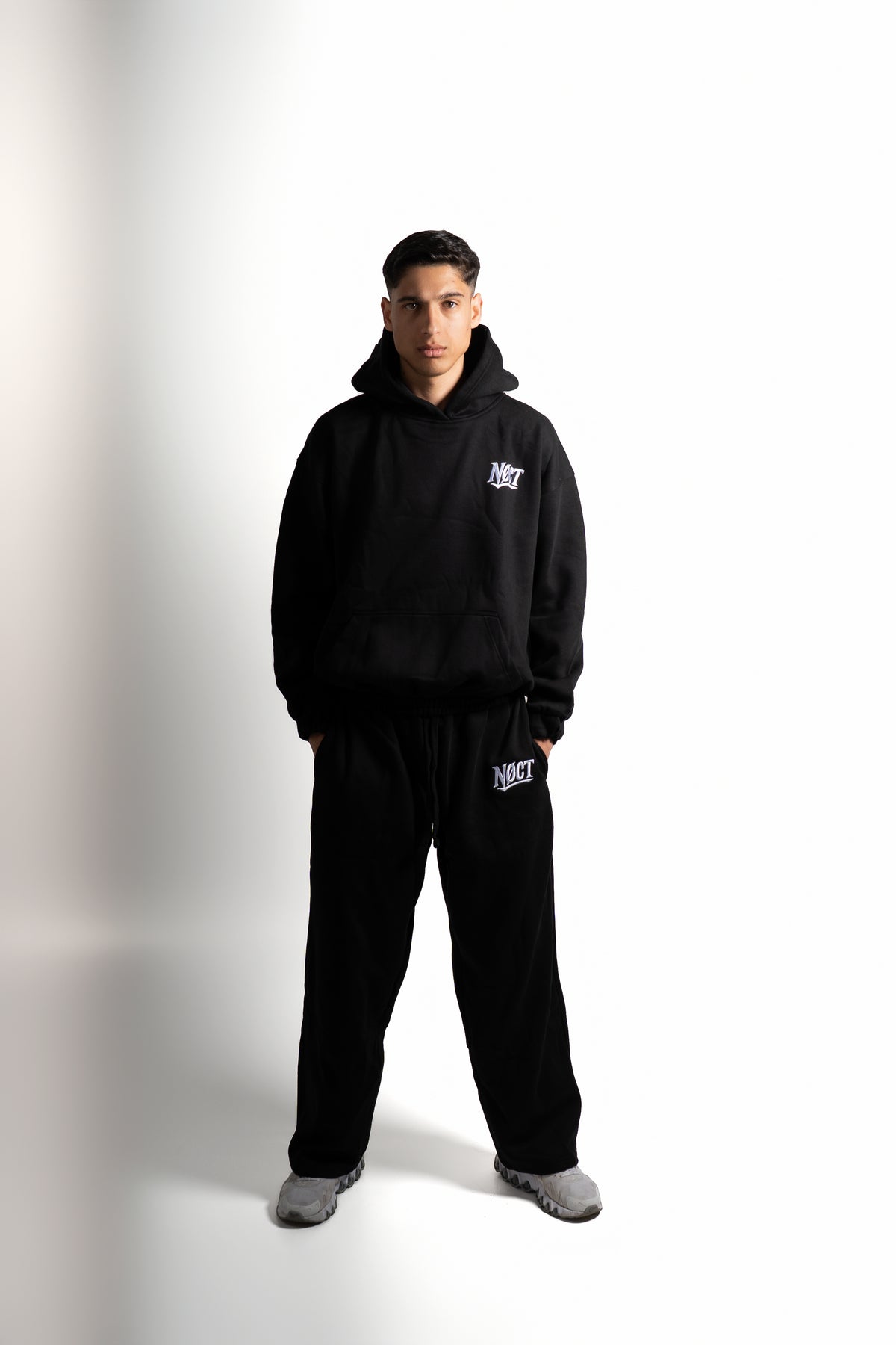 NØCT Essential Tracksuit in Schwarz: Model mit Hoodie und weiter Sweatpants